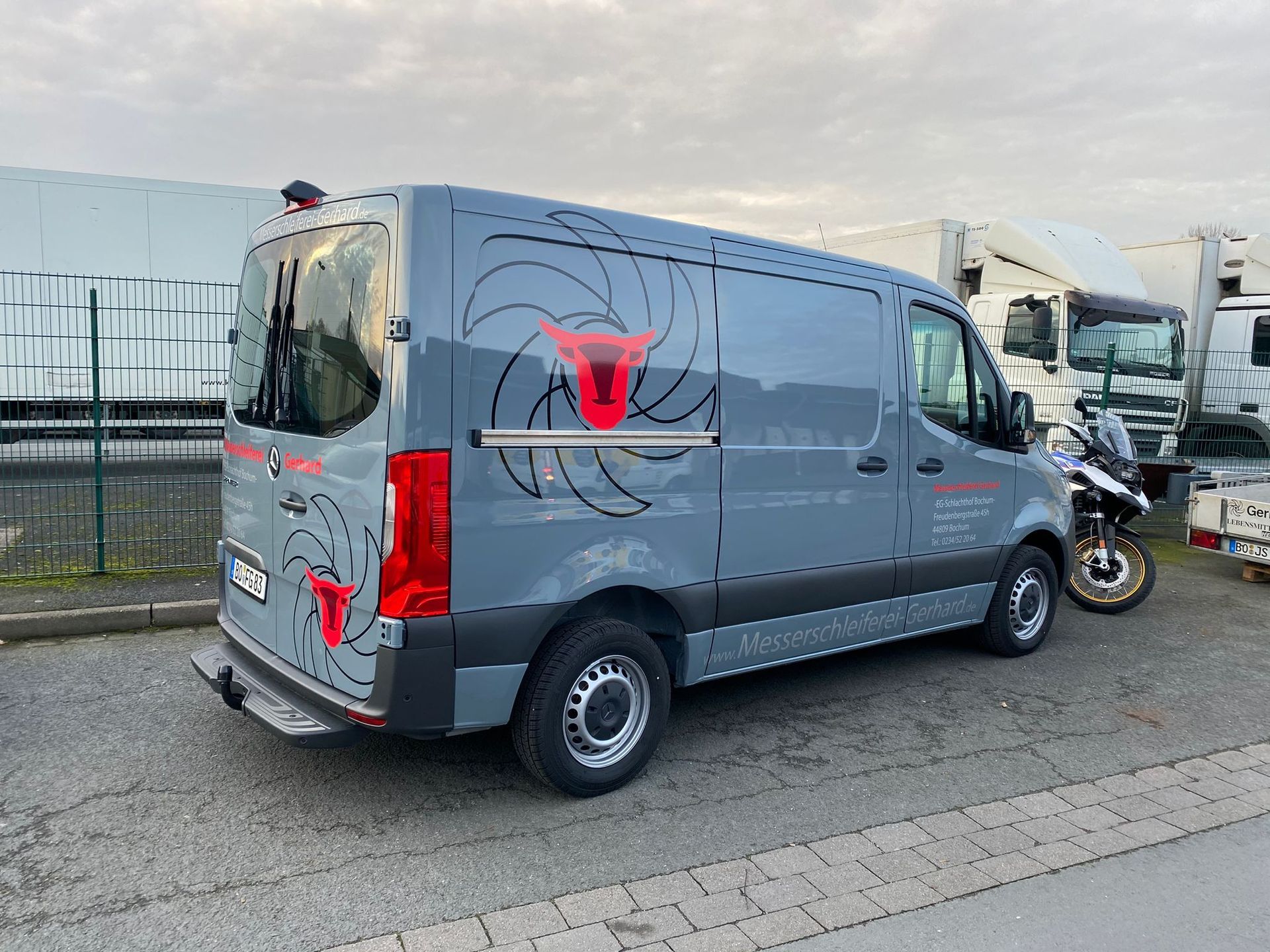 Ein grauer Lieferwagen parkt am Straßenrand neben einem Motorrad.