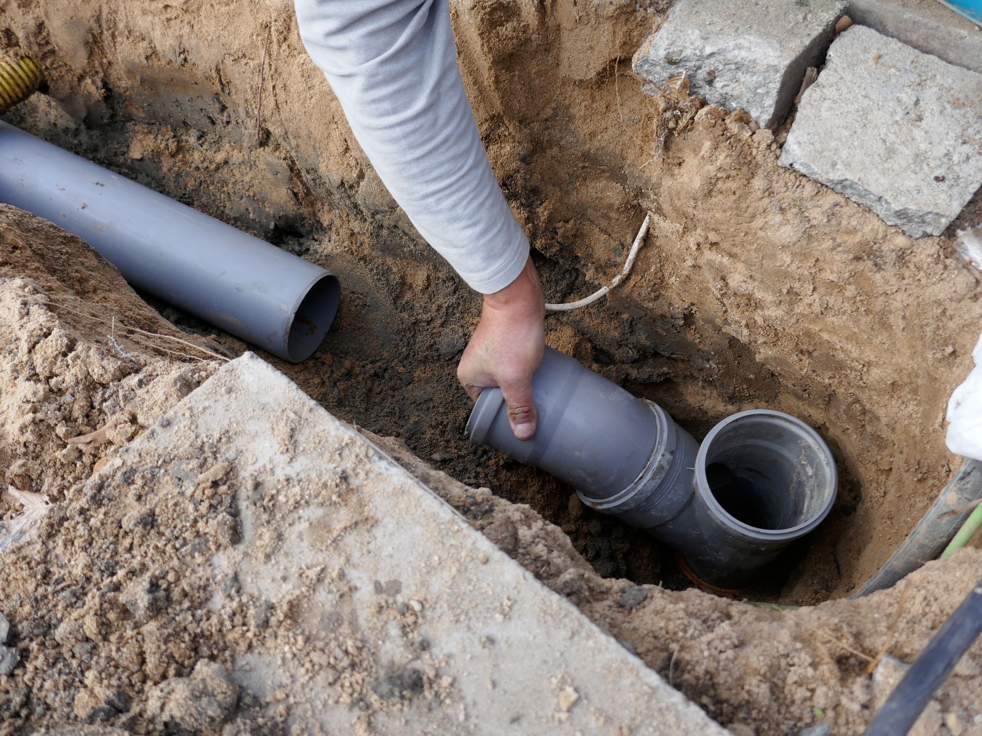 Une personne en train de tenir un tuyau de canalisation en PVC dans une tranchée.