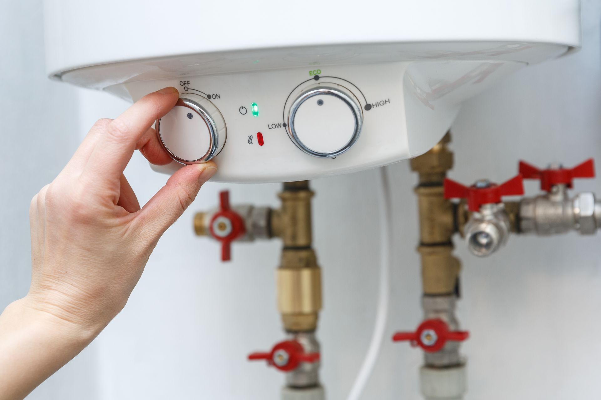 Main en train de tourner le bouton gauche d'un chauffe-eau électrique.