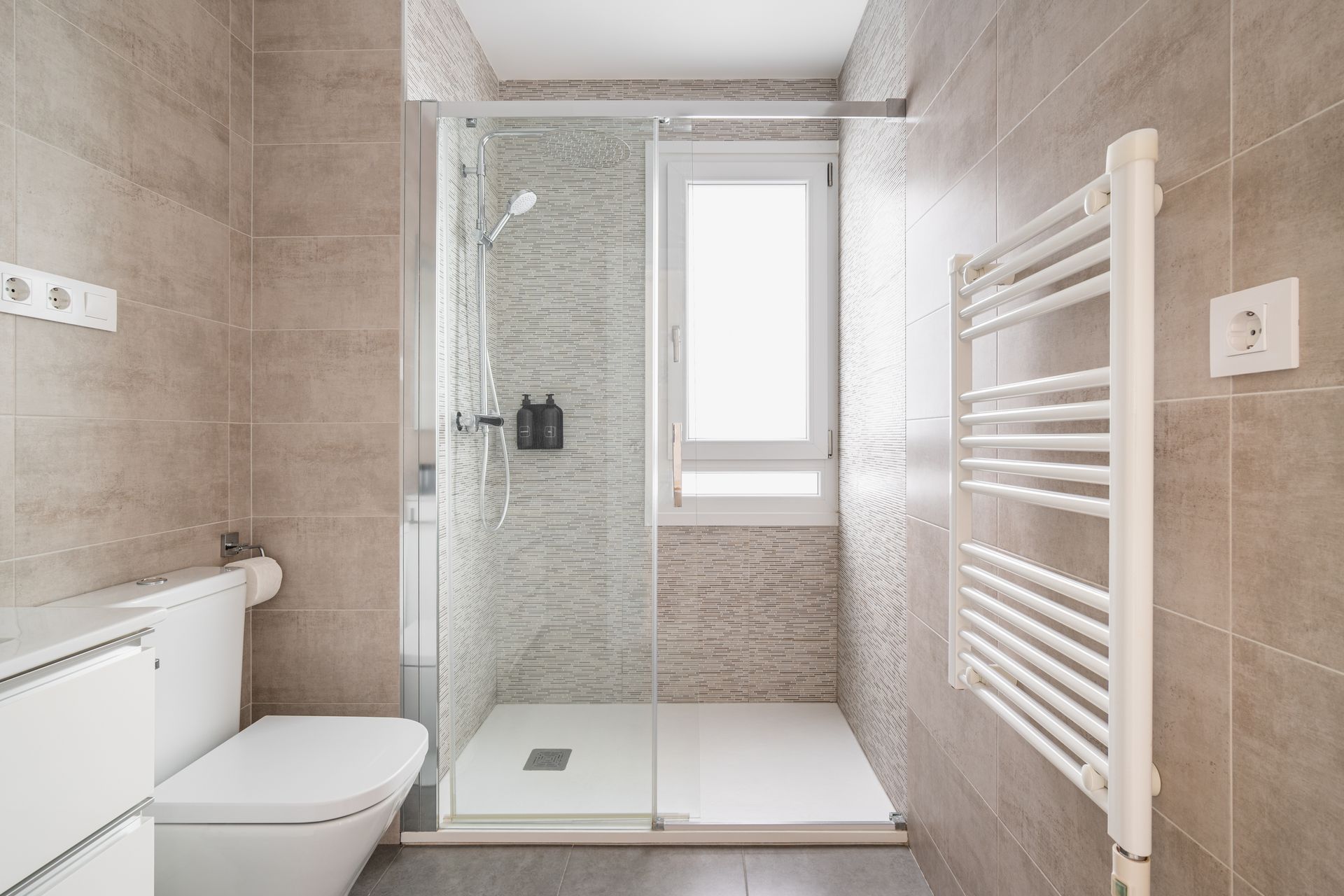 Douche à l'italienne au fond d'une salle de bains avec toilettes et sèche-serviettes.