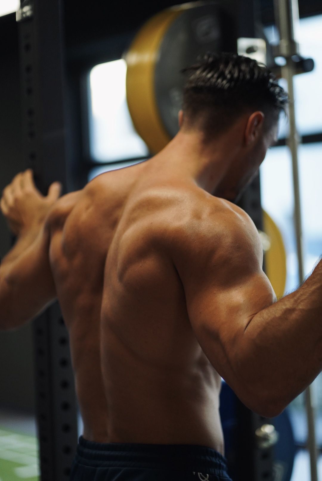 Ein Mann ohne Hemd stemmt in einem Fitnessstudio Gewichte.