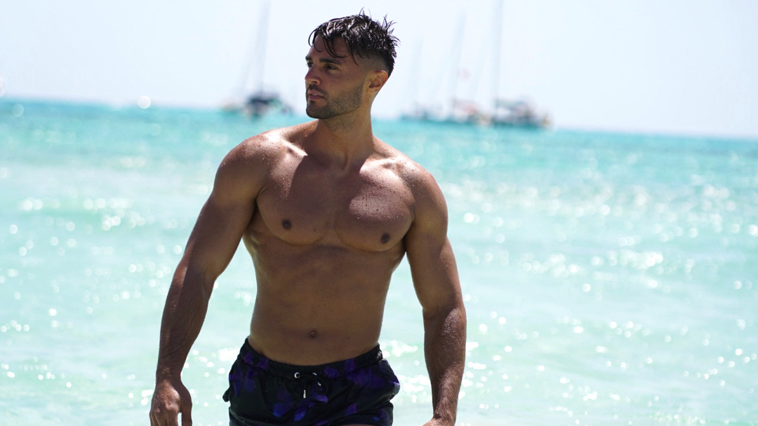 Ein Mann ohne Hemd steht an einem Strand in der Nähe des Meeres.