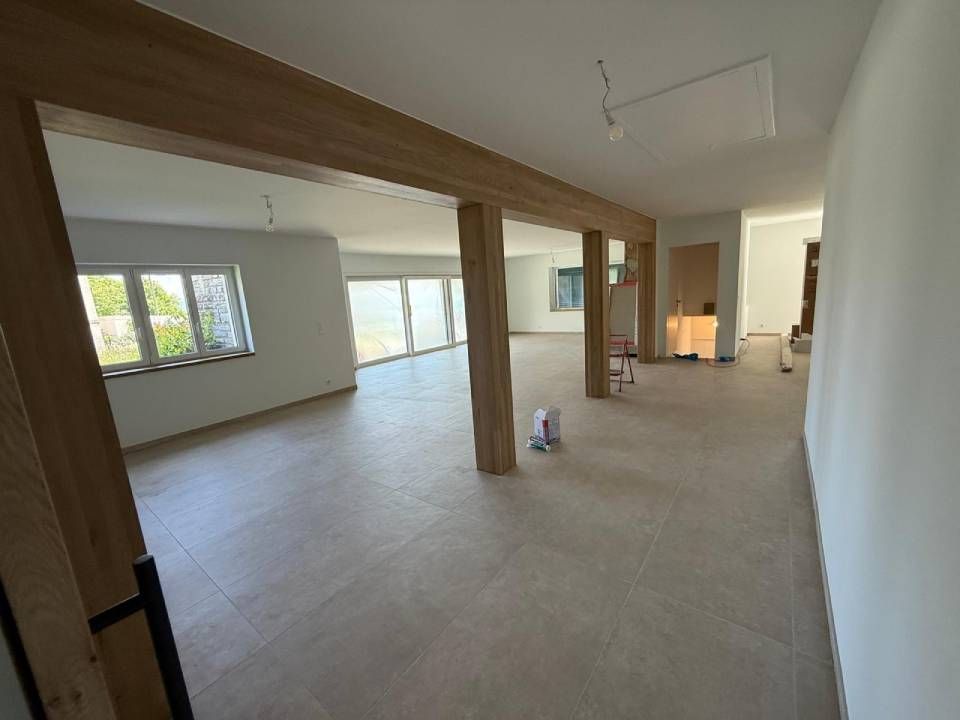 Intérieur vide avec poutres et piliers en bois clair, grandes fenêtres et sol neutre.