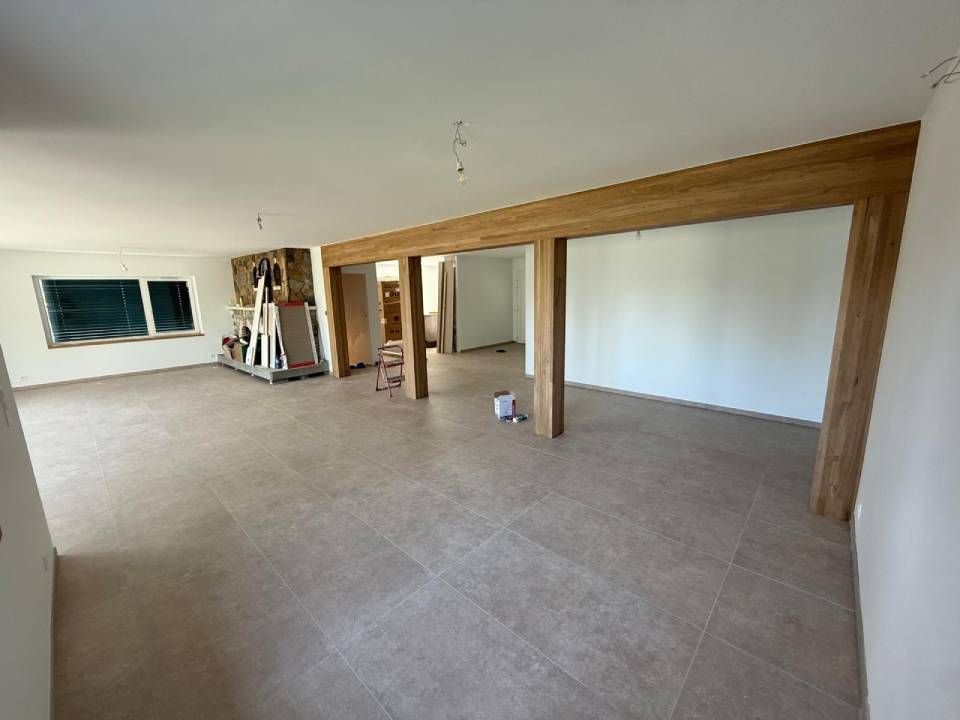 Intérieur rénové avec poutres en bois, sol carrelé et murs blancs.