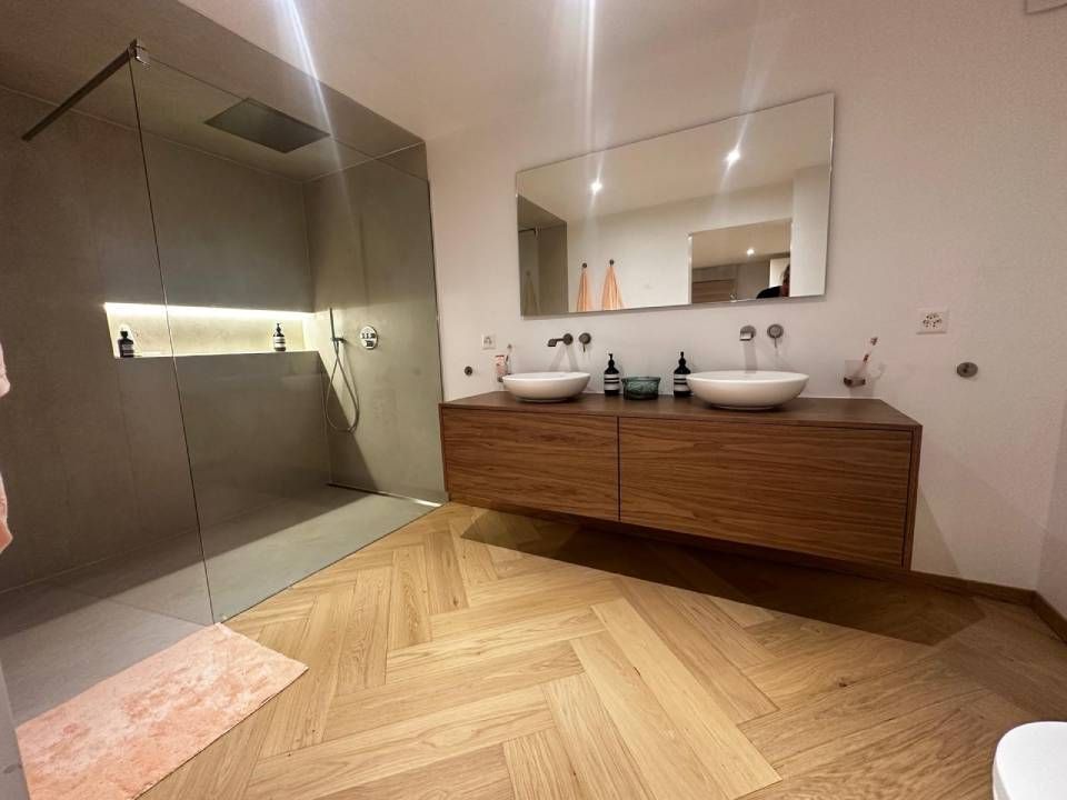 Salle de bains moderne avec meubles en bois, vasques à poser, grand miroir et parquet à chevrons.