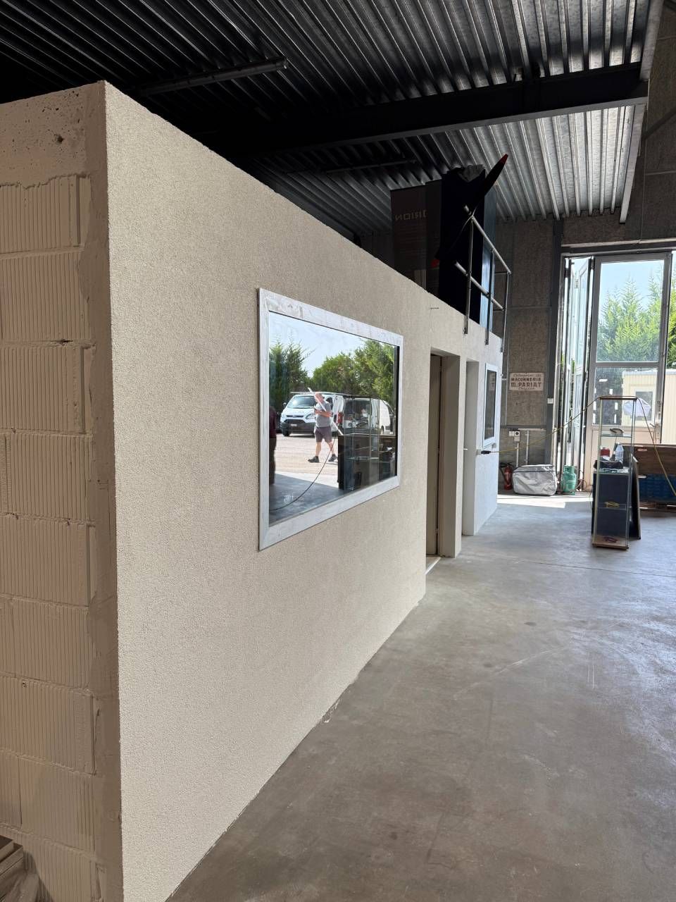 Vue intérieure d'un bâtiment industriel montrant un mur plâtré, une fenêtre et une porte.