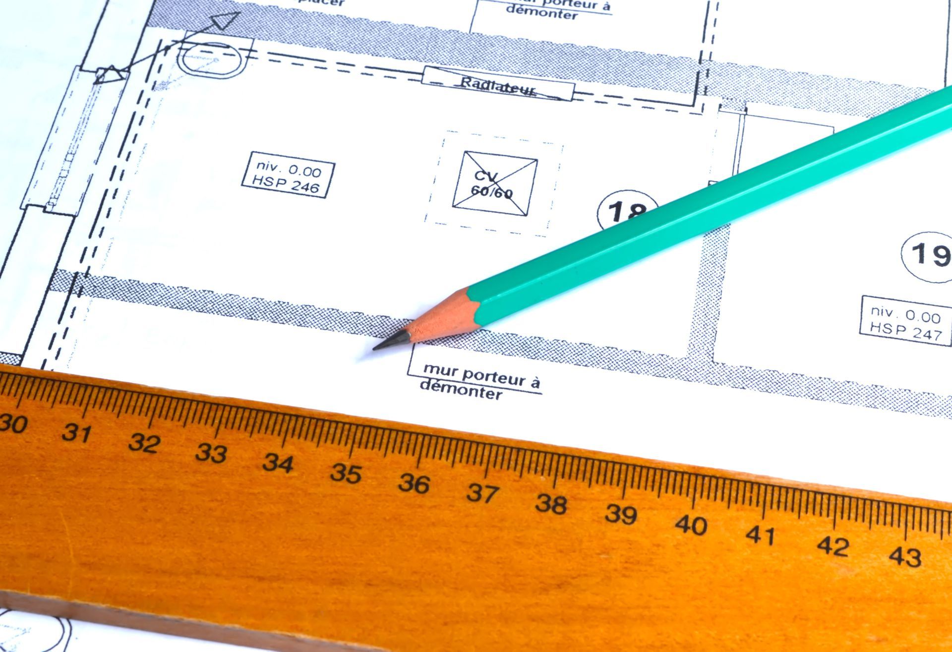Un crayon désigne un plan d'étage sur un plan d'architecte, une règle en bois étant posée en bas de la page.