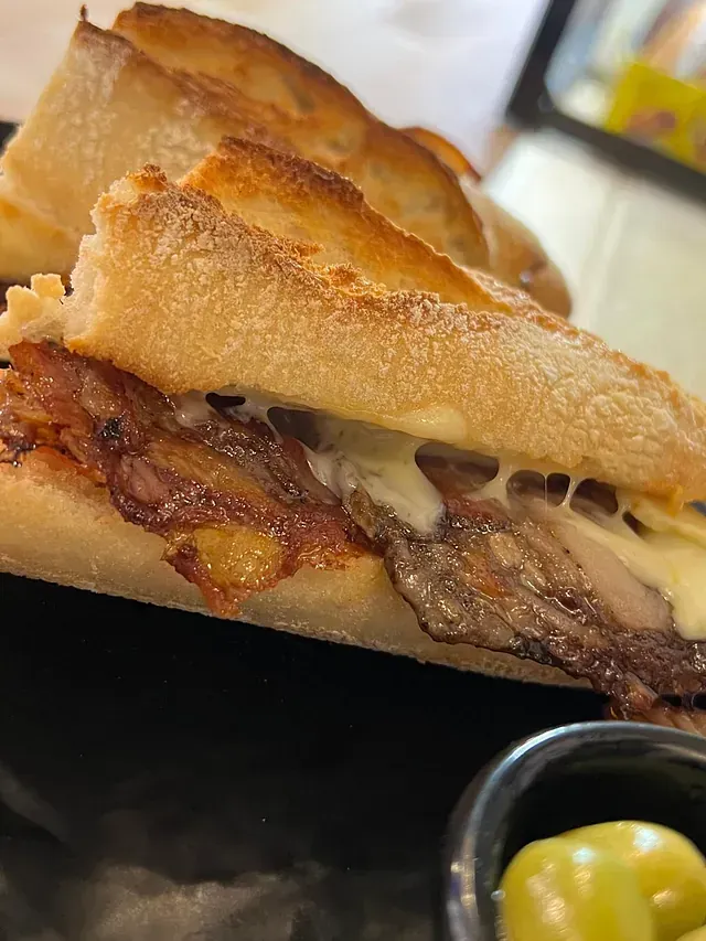 Un primer plano de un sándwich en un plato junto a un tazón de aceitunas.