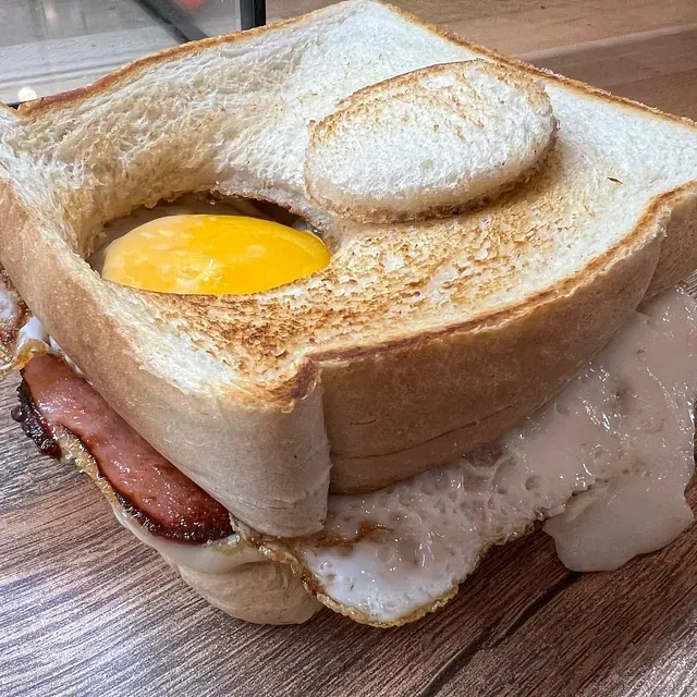 Un sándwich con huevos, tocino y queso en una mesa de madera.