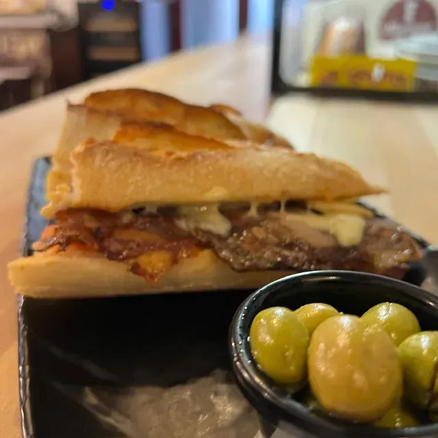 Un sándwich está sobre una mesa al lado de un bol de aceitunas.