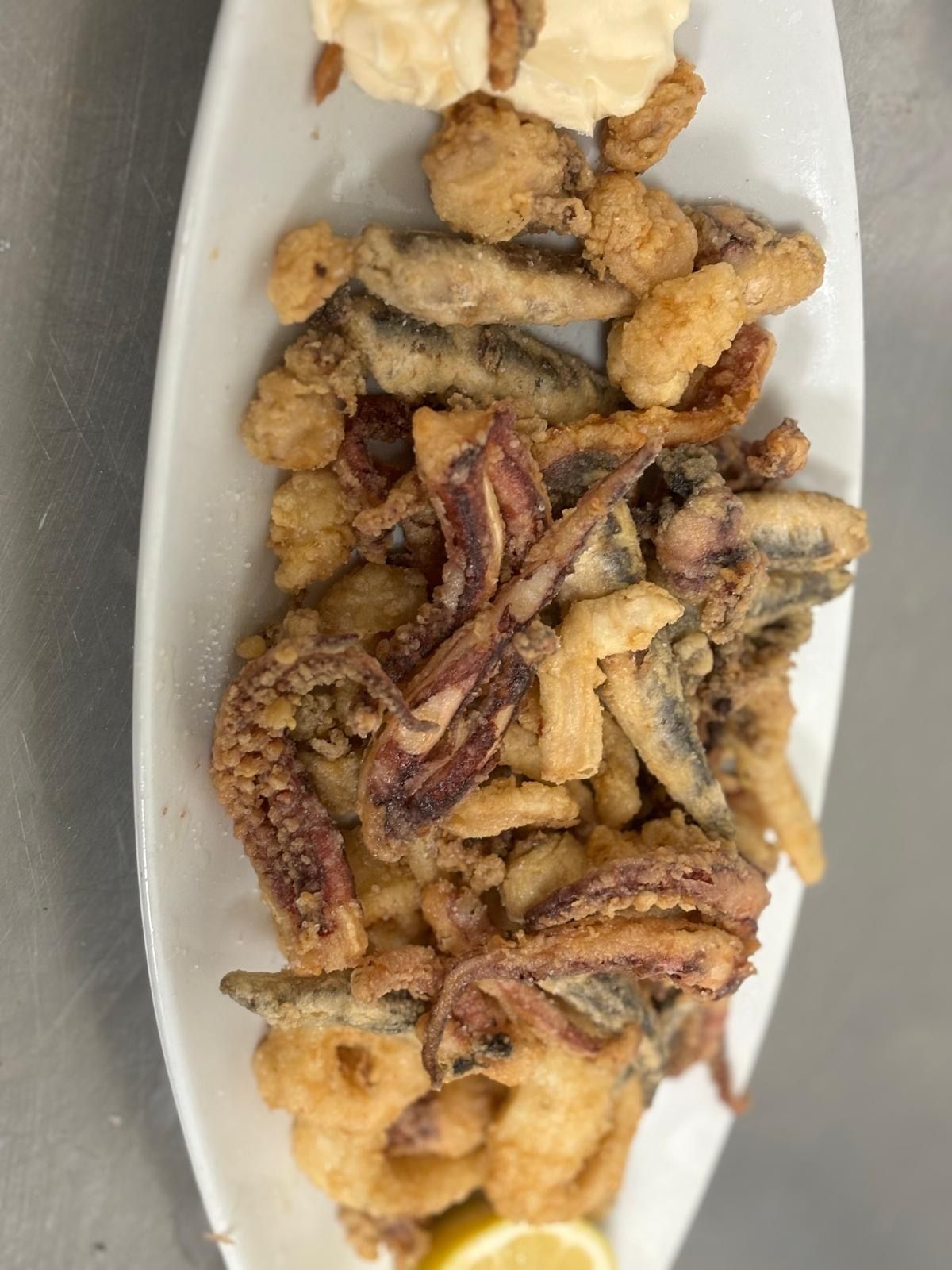 Un plato blanco cubierto con mariscos fritos y una rodaja de limón.
