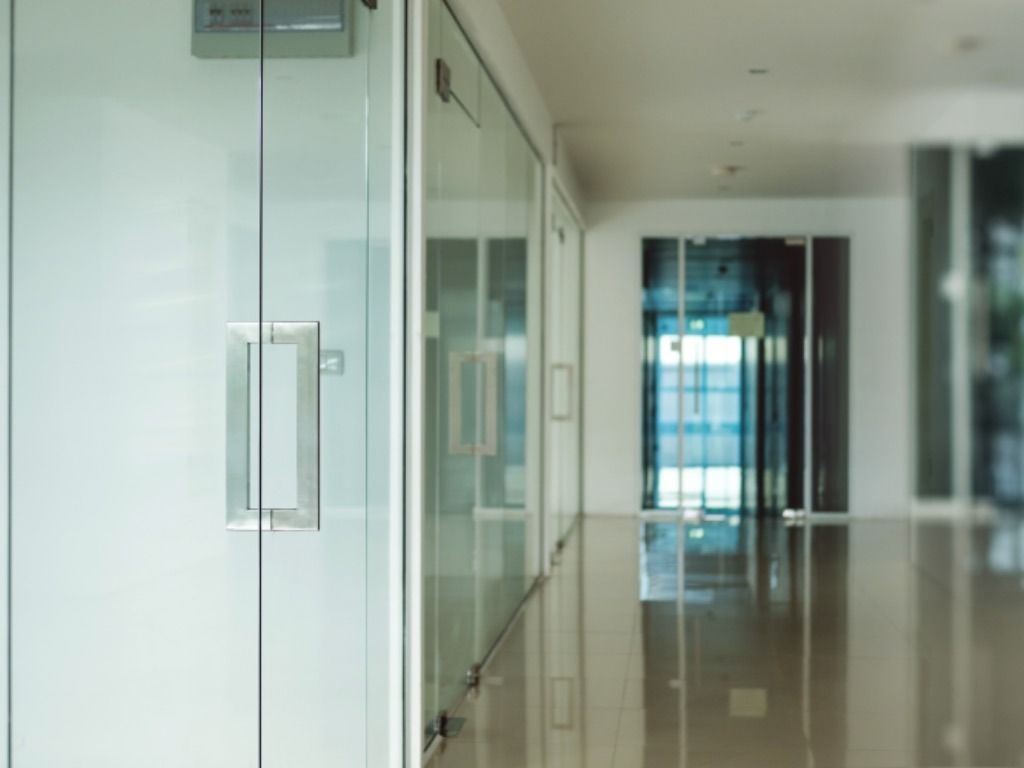 Un pasillo con paredes y puertas de vidrio en un edificio de oficinas.