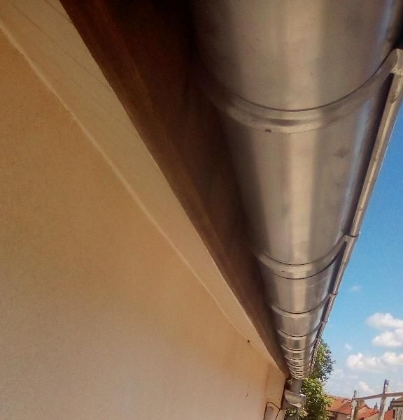 Gros plan sur une gouttière en métal argenté le long d'un mur beige, avec un ciel bleu visible.