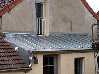 Ajout d'une toiture en métal galvanisé sur un bâtiment avec un balcon au-dessus.