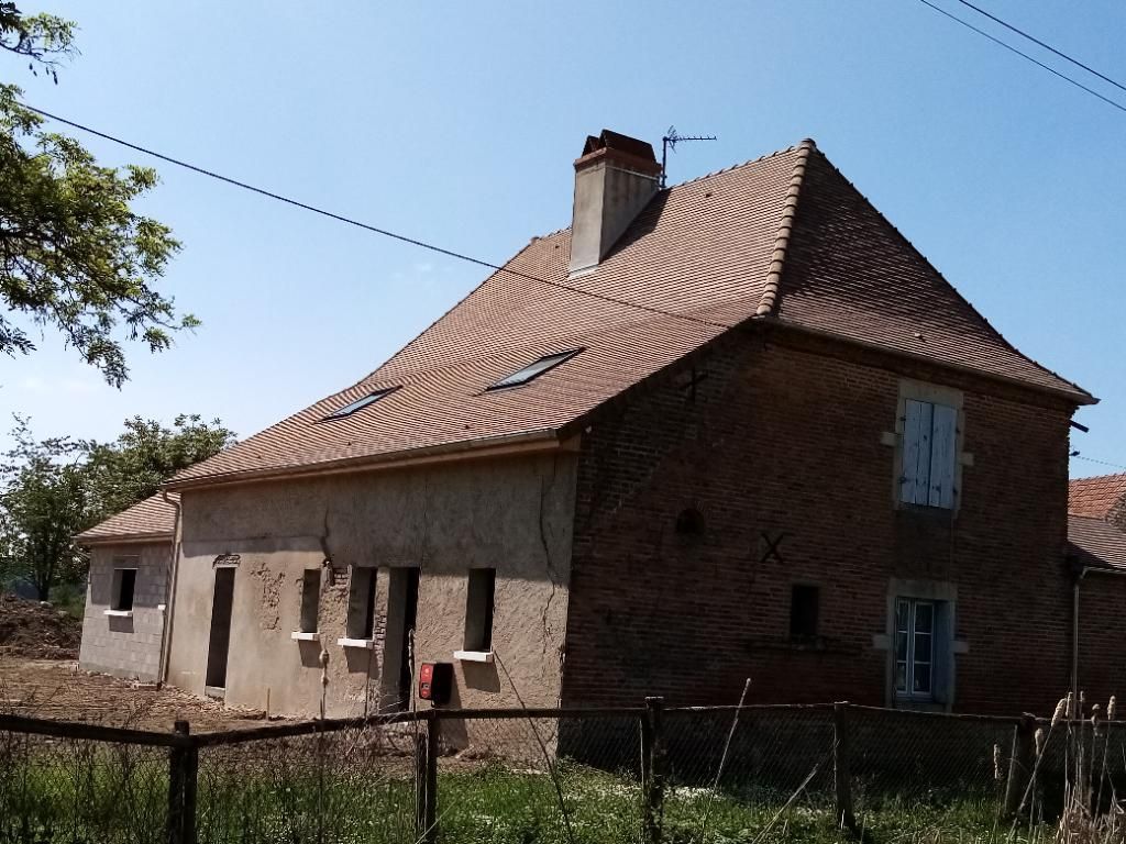 Maison en briques avec toit de tuiles rouges, en cours de rénovation. Elle comprend des fenêtres, une cheminée et une petite extension.
