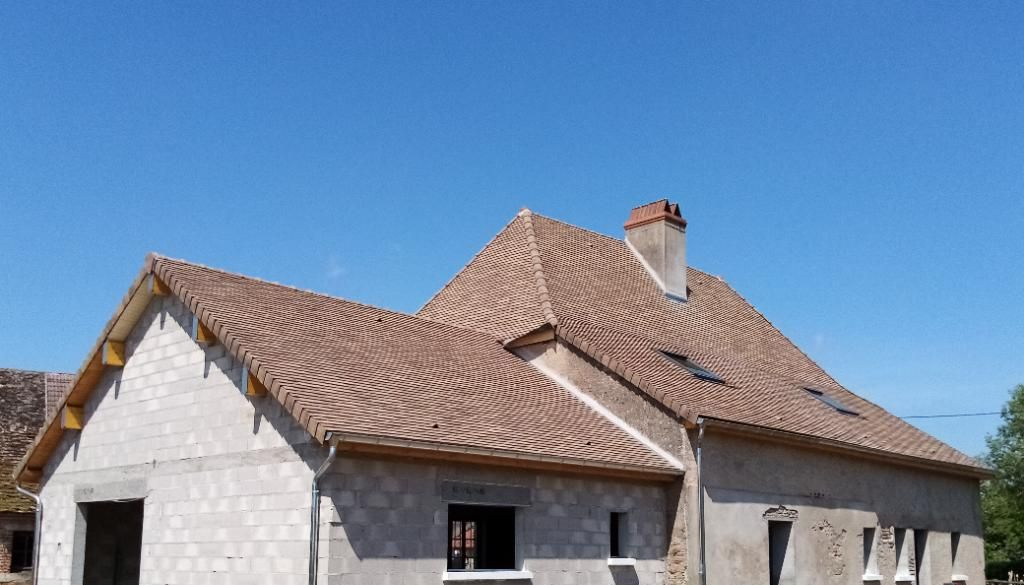 Maison en construction avec un toit de tuiles brunes sous un ciel bleu.