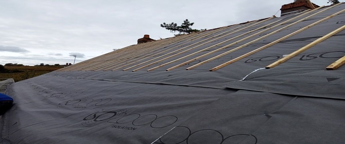 Une main gantée dépose une tuile en terre cuite sur un cadre en bois.