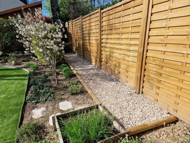 Jardin avec allée gravier le long de la clôture en bois.