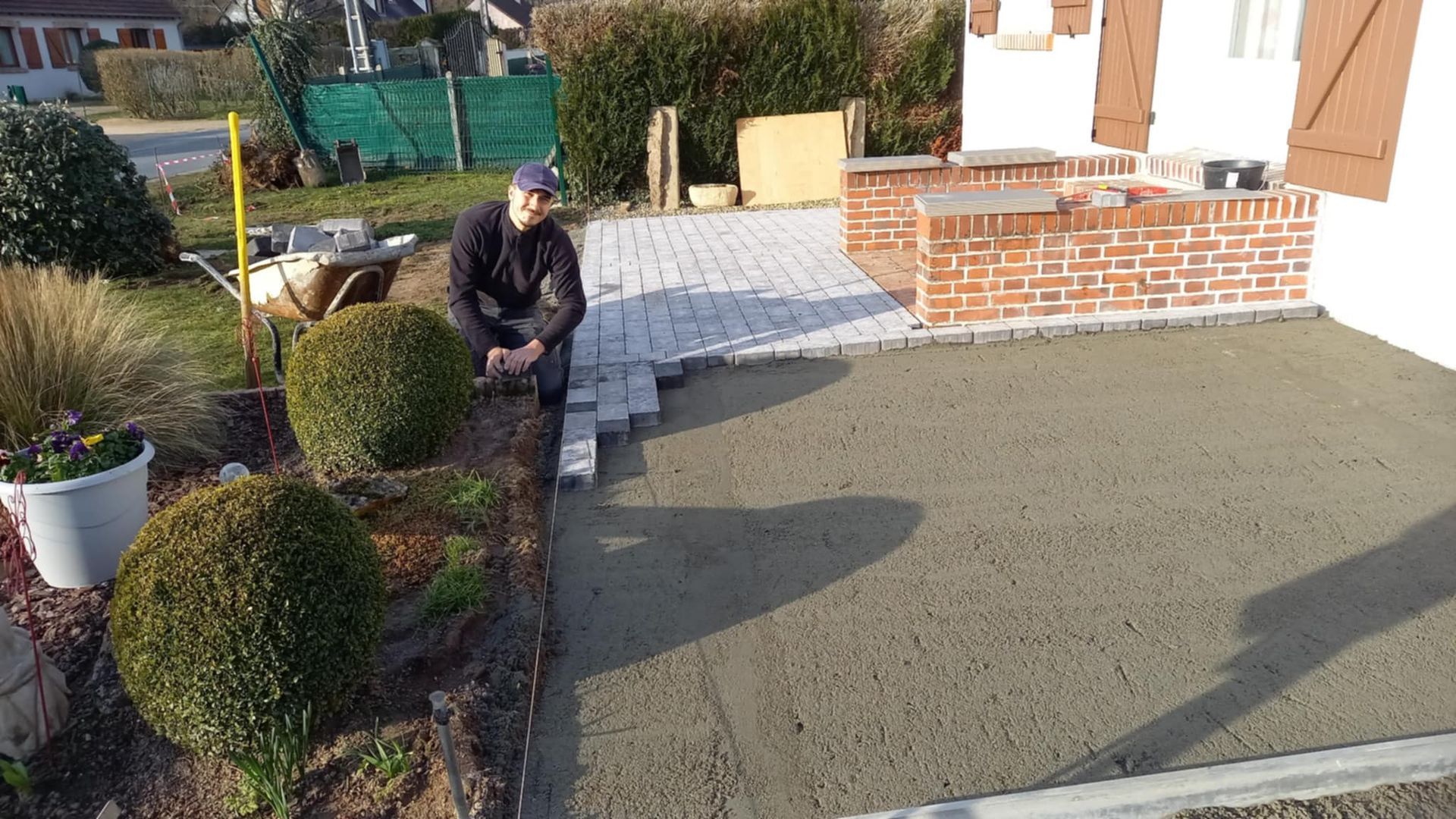 Un ouvrier pose des pavés autour de l'escalier d'une maison.