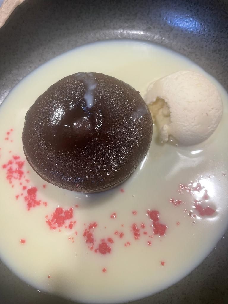 Un pastel de chocolate fundido servido en un tazón de salsa blanca con una bola de helado de vainilla y una pizca de polvo rojo.