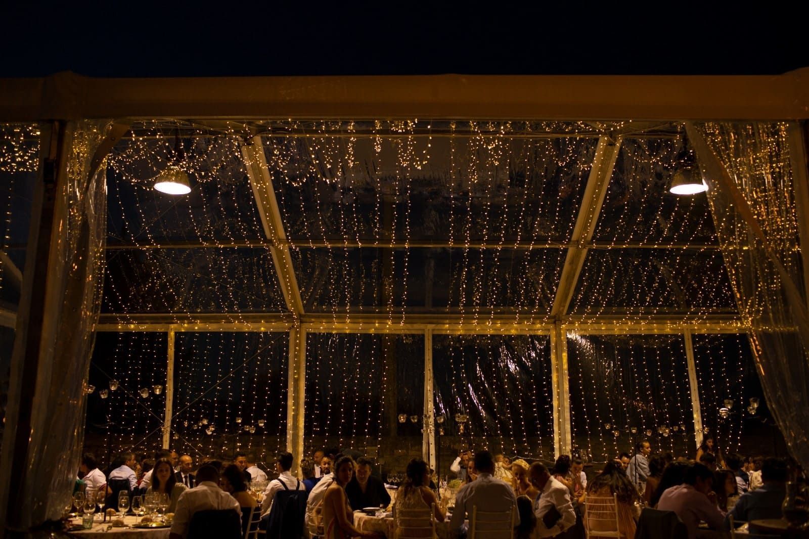 La gente estaba sentada a las mesas del comedor bajo un techo transparente tipo carpa, adornado con guirnaldas de luces cálidas que colgaban en cascada.