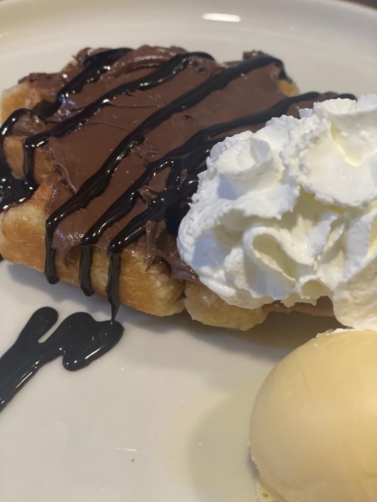 Un gofre belga cubierto con crema de chocolate, sirope de chocolate, nata montada y una bola de helado de vainilla.
