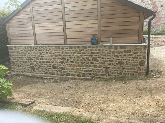 Structure extérieure en pierre et en bois avec une petite statue centrée sur le mur.