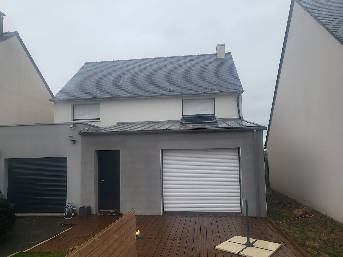 Petite maison avec porte de garage et terrasse en bois humide entre deux maisons voisines.