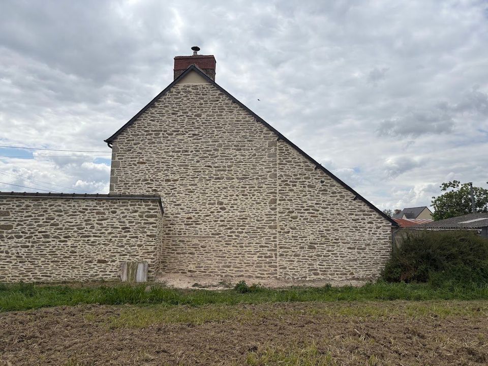 Mur à pignon en pierre avec une cheminée, à côté d'un champ et d'un muret en pierre basse.