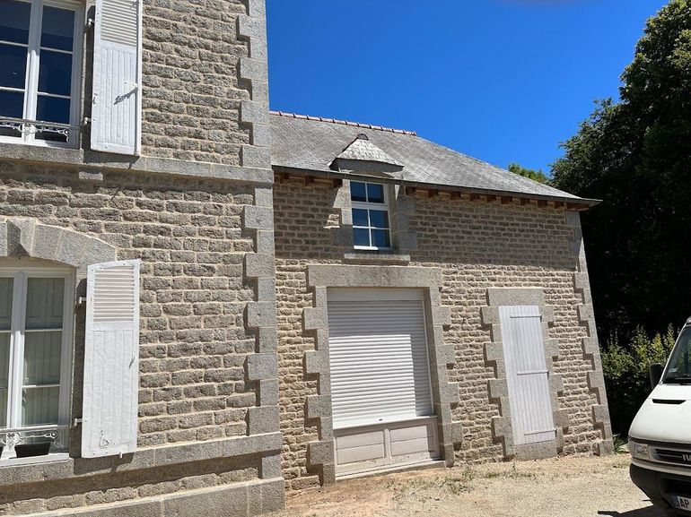 Bâtiment en pierre avec volets et porte de garage.
