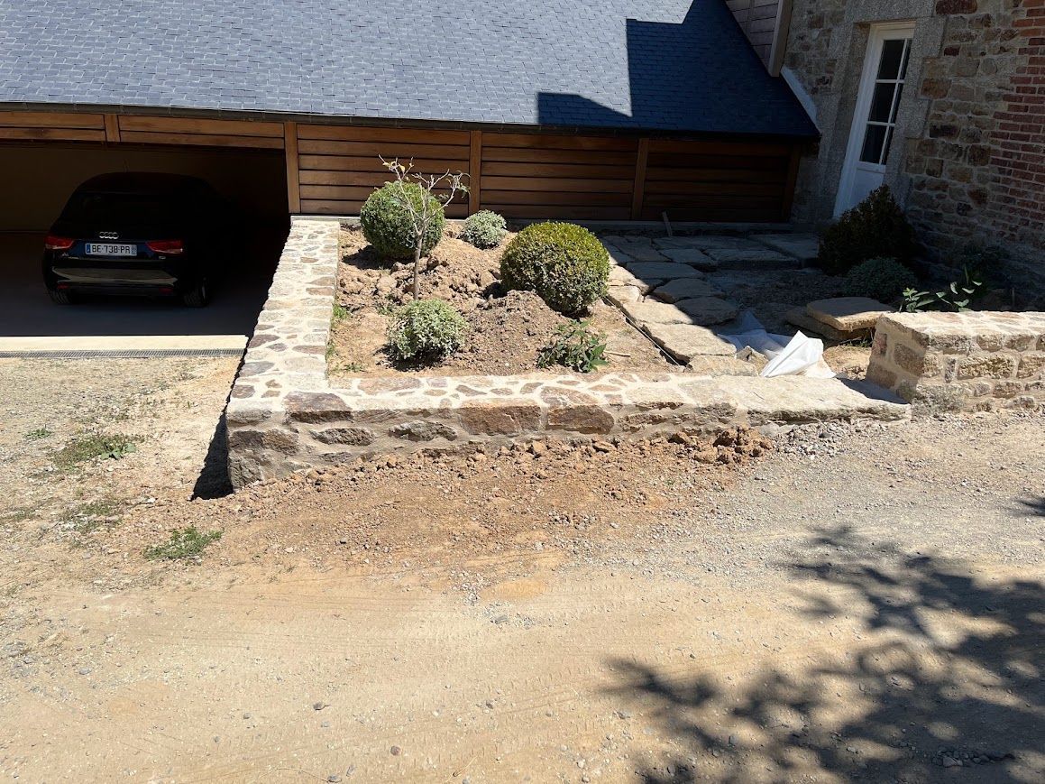 Mur de soutènement en pierre et petite jardinière paysagée à côté de l'allée d'un garage.
