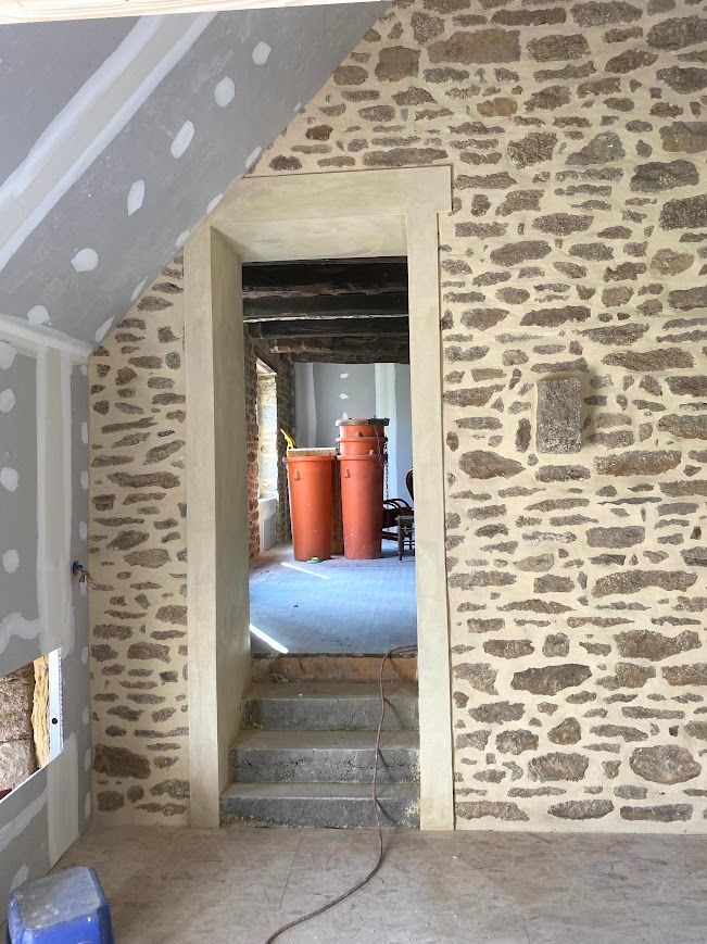 Couloir intérieur aux murs de pierre avec une petite porte menant à des cylindres dans une pièce.