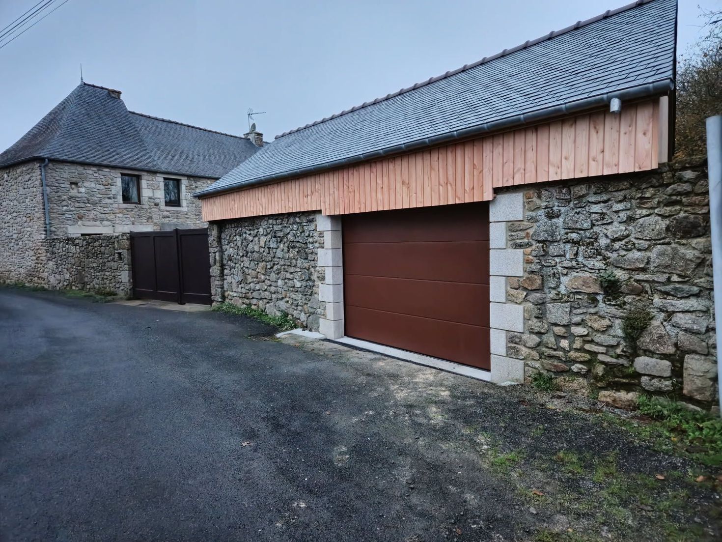 Bâtiments en pierre avec toits d'ardoise au bord d'une route pavée et une porte de garage.