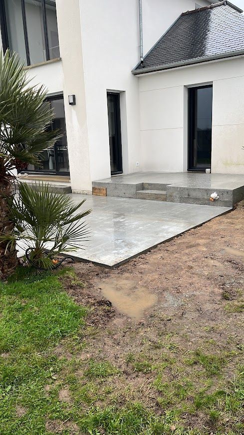 Extérieur de maison moderne avec terrasse couverte, murs, portes et petit jardin.
