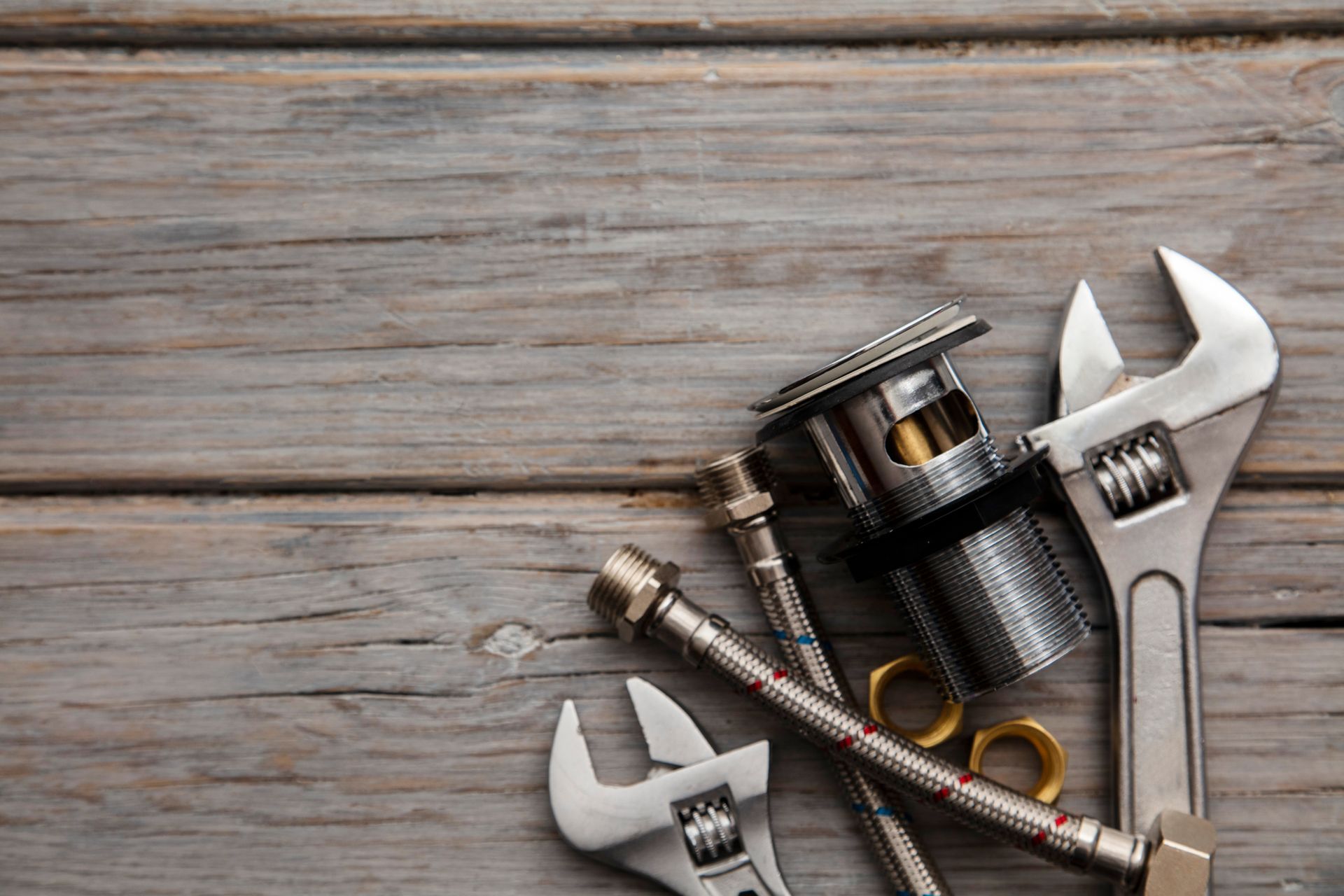 Outils de plomberie : clés réglables, composants de drainage, tuyau flexible et raccords en laiton sur une surface en bois patiné