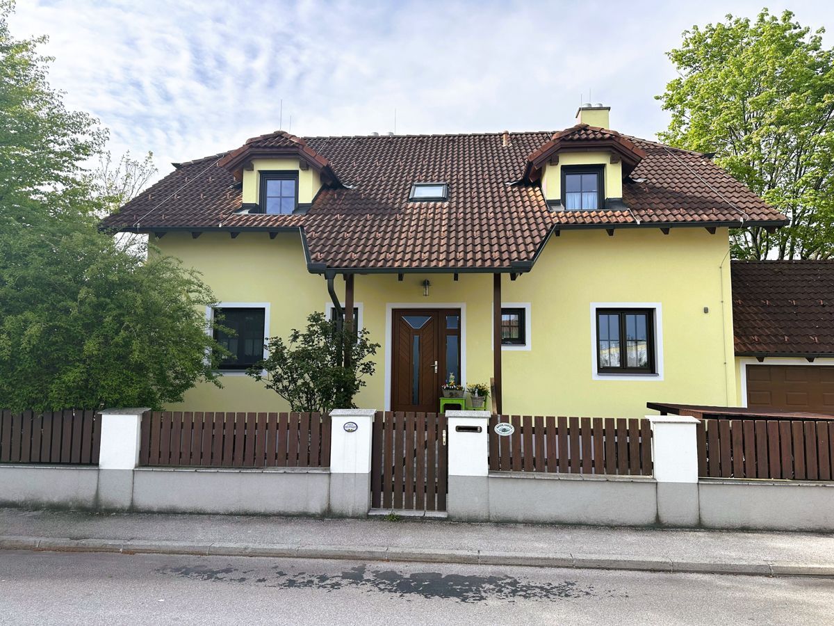 Ein gelbes Haus mit einem braunen Dach und einem Holzzaun