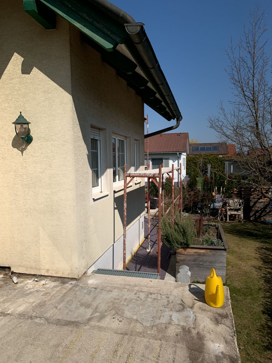 Eine gelbe Gießkanne steht vor einem Haus
