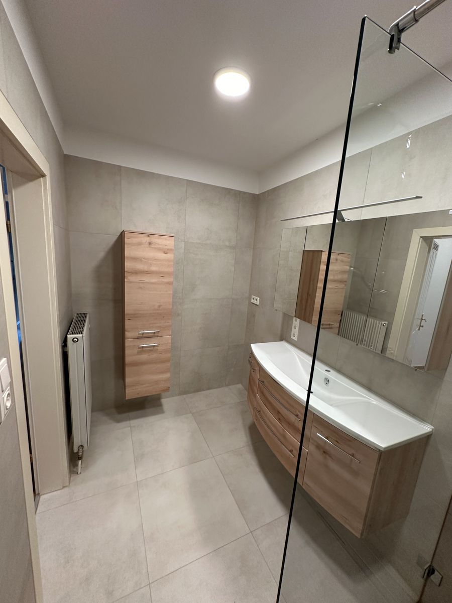 Ein Badezimmer mit Waschbecken, Spiegel und ebenerdiger Dusche.