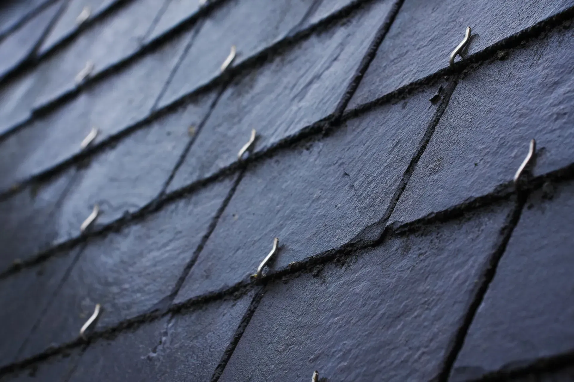 Tuiles de toit en ardoise gris foncé avec fixations métalliques.