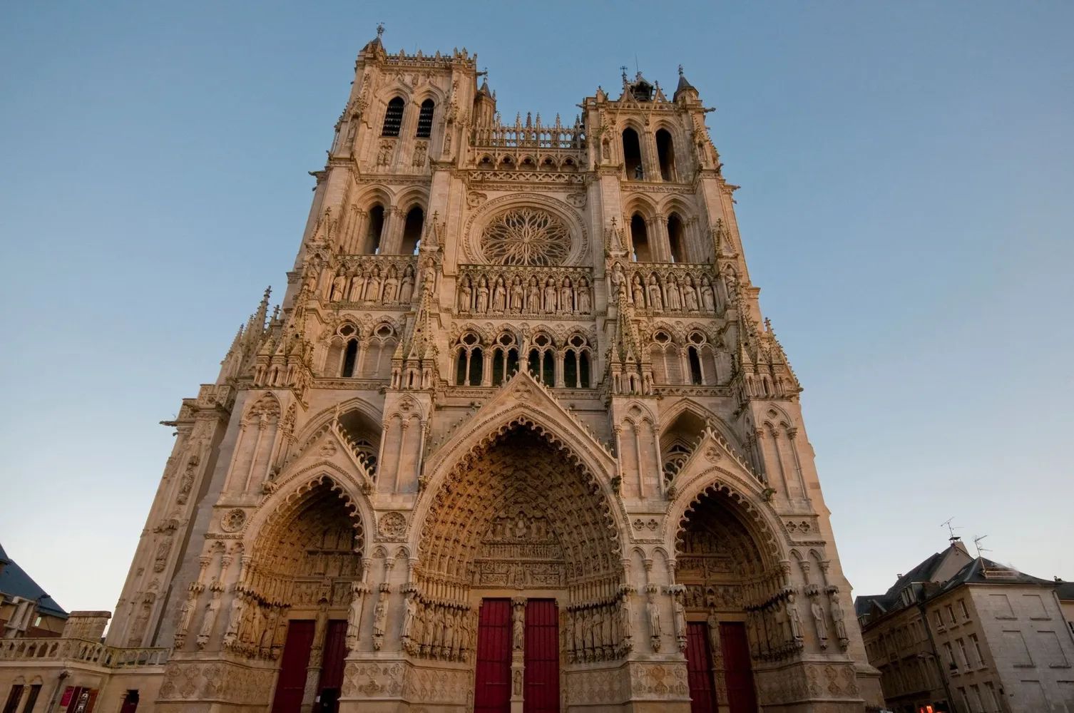 Façade de cathédrale gothique ornée de sculptures détaillées et d'une rosace, sous un ciel d'un bleu limpide.