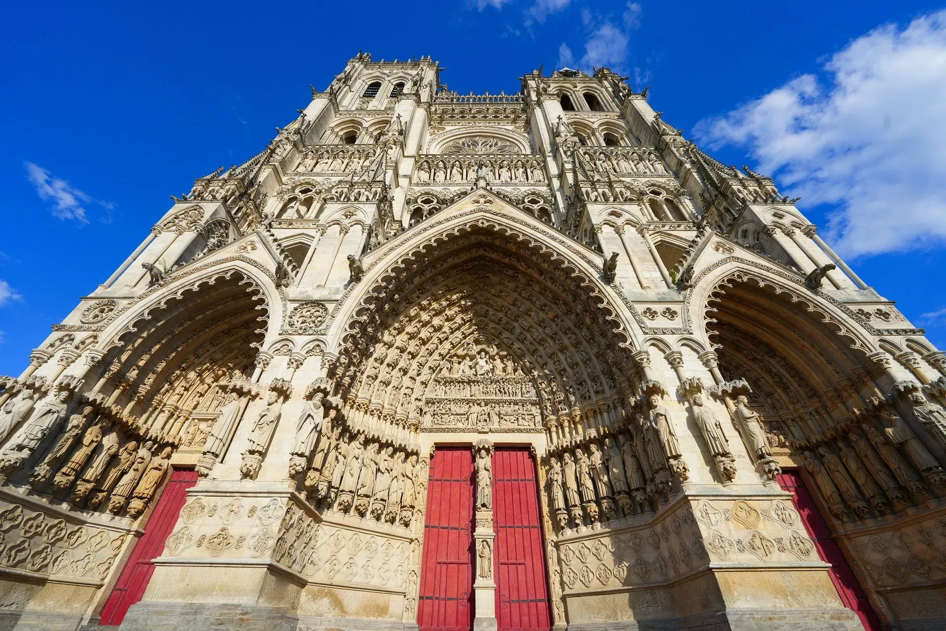 La cathédrale d'Amiens, avec sa façade ornée, ses portes rouges et son ciel bleu.