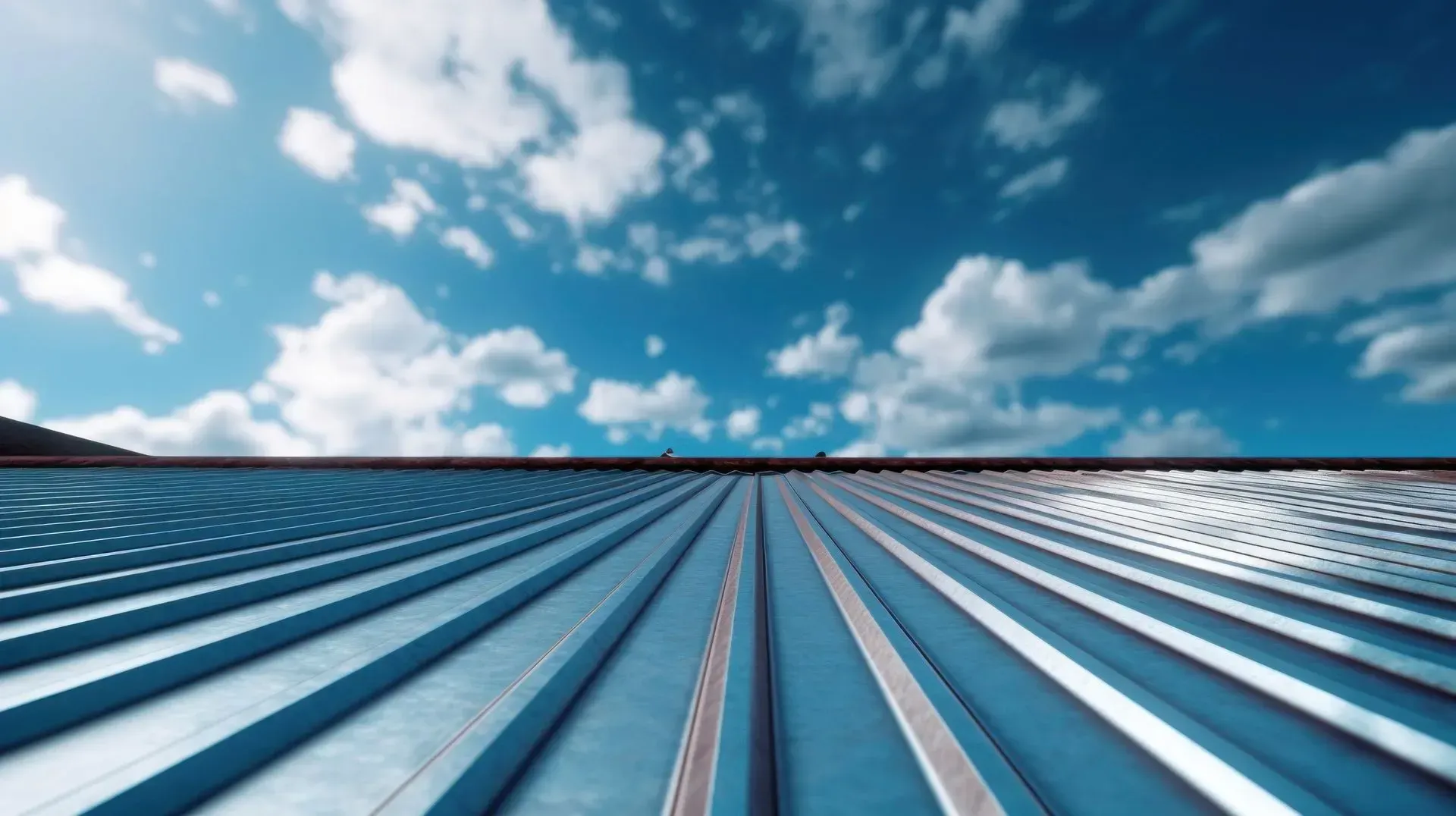 Toiture métallique bleue inclinée vers un ciel bleu vif parsemé de nuages ​​blancs duveteux.