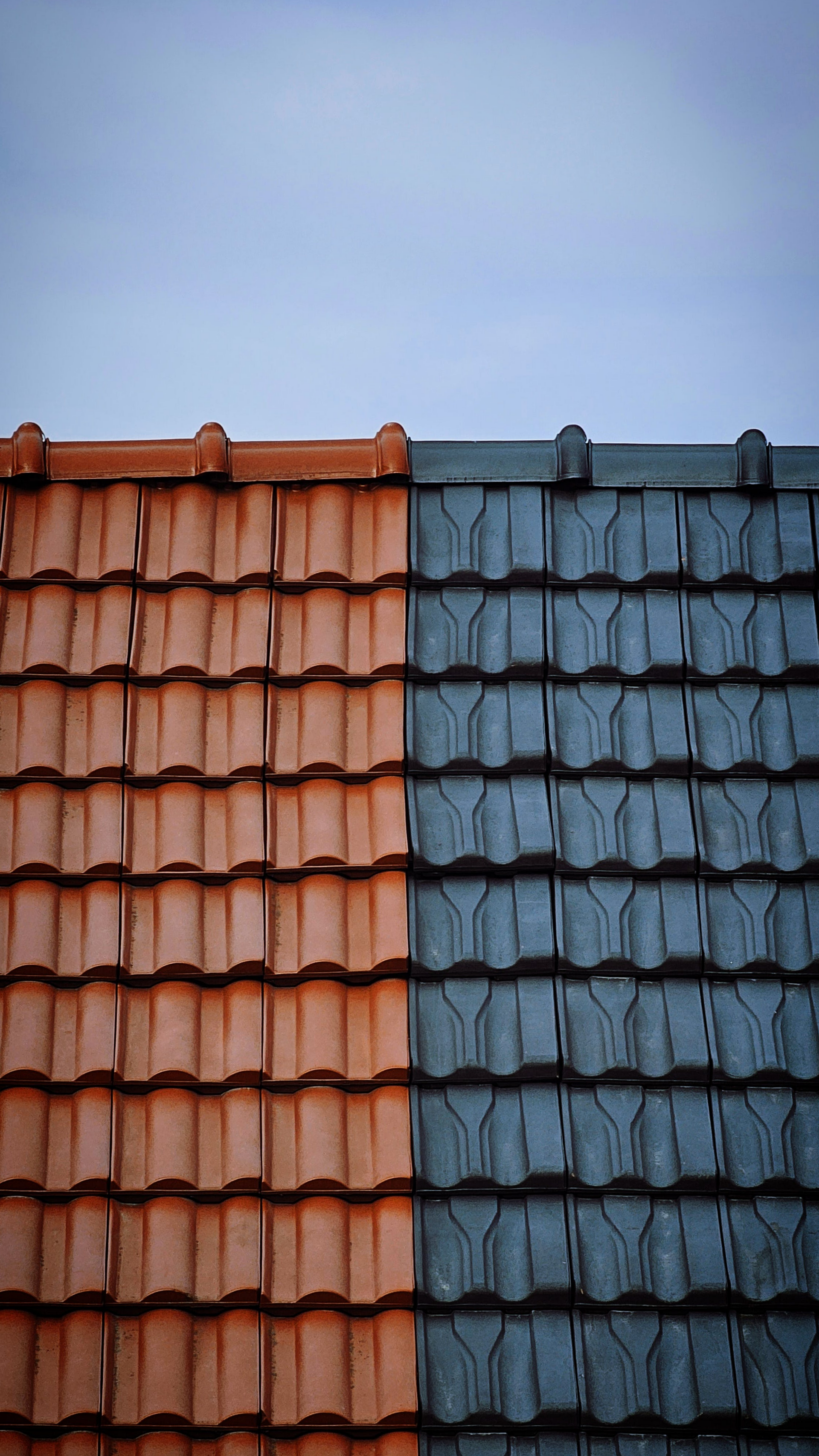 Toit mi-tuile orange, mi-tuile grise, sur un ciel bleu pâle.