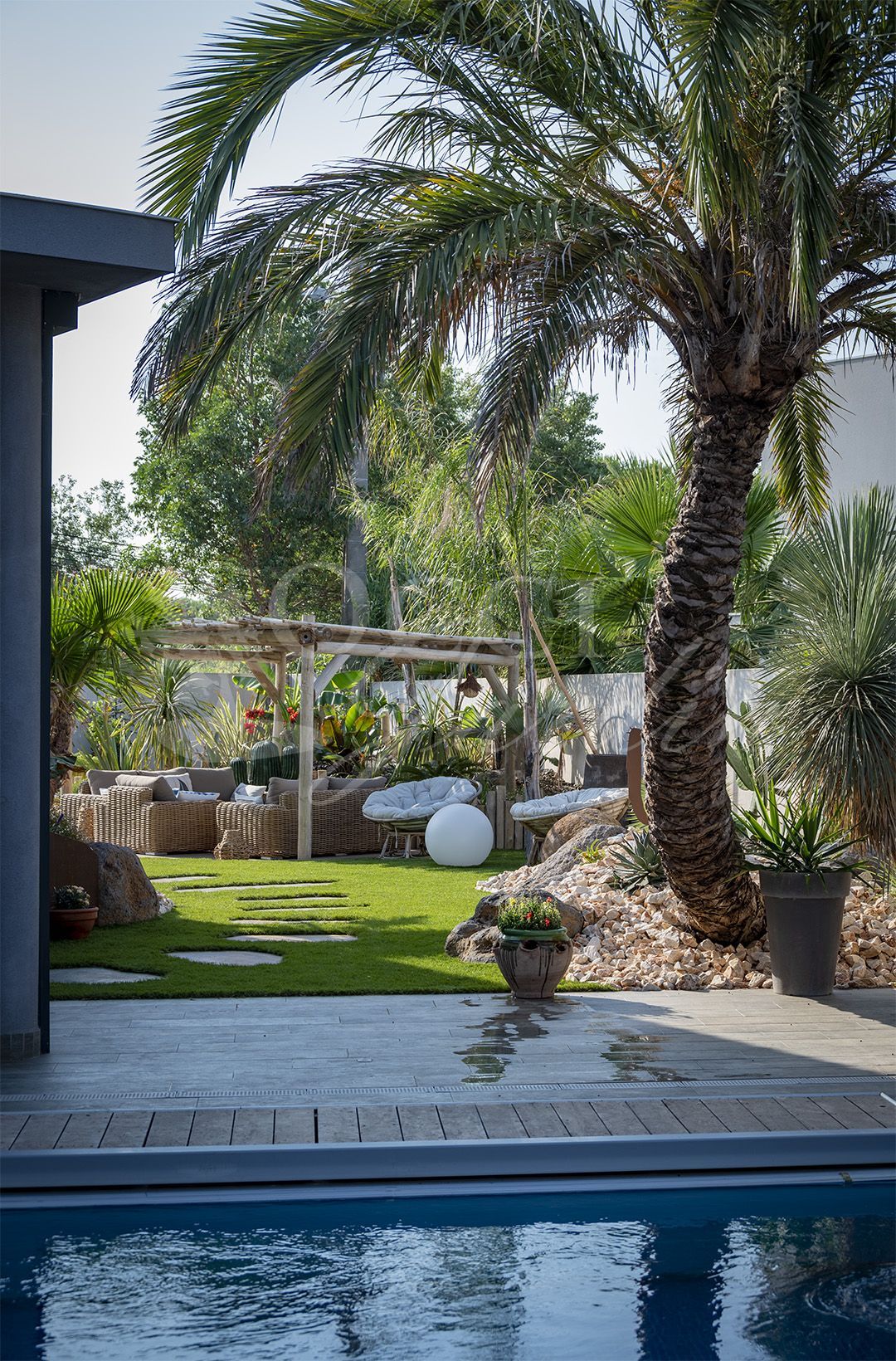 Jardin avec piscine, palmier et coin salon sous une pergola.