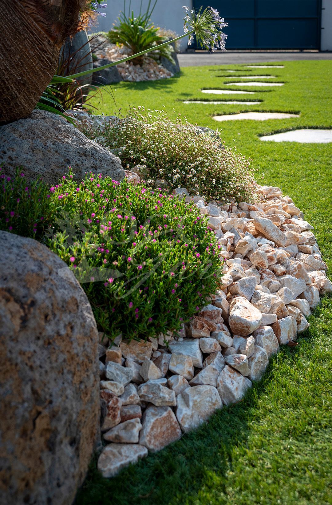 Jardin de rocaille avec arbustes verts, pierres et pelouse.