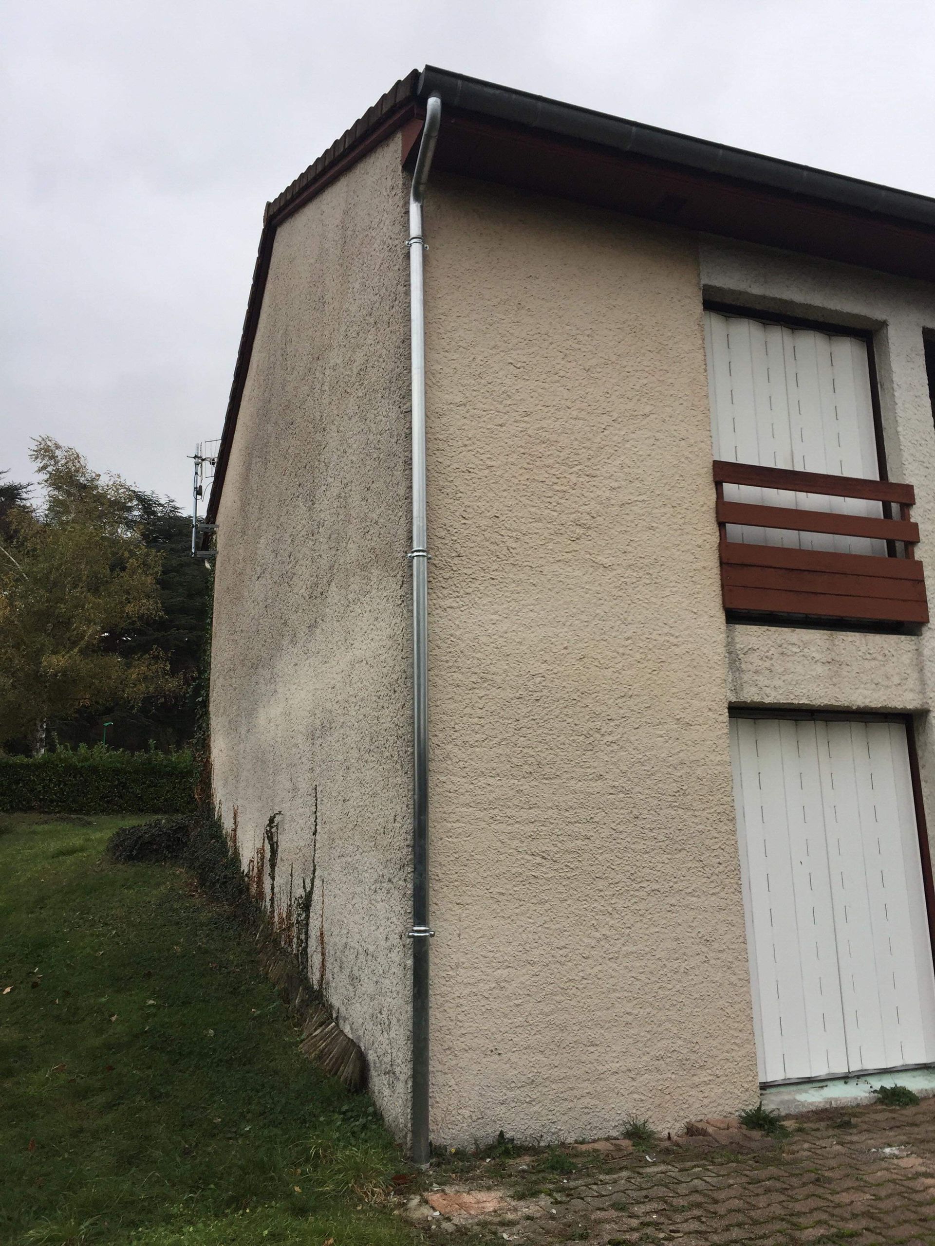 Vue latérale d'une maison en stuc beige avec une porte blanche et un petit balcon en bois.