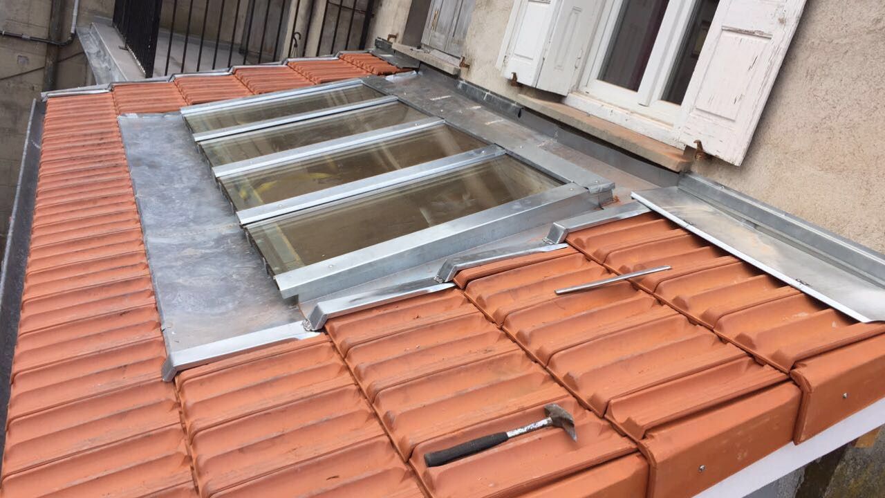 Toiture en construction avec tuiles rouges et charpente métallique apparente près d'une fenêtre.