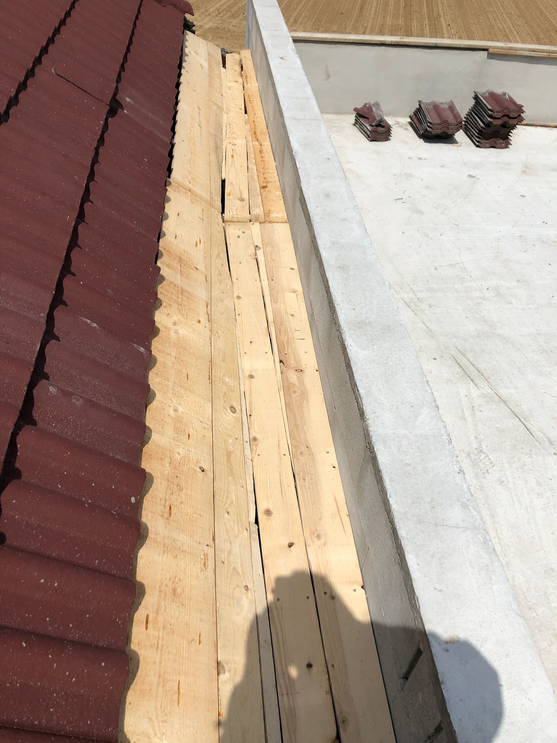 Réparation d'un joint de toiture à côté d'une toiture métallique rouge et d'une toiture plate blanche, avec sous-couche en bois apparente.