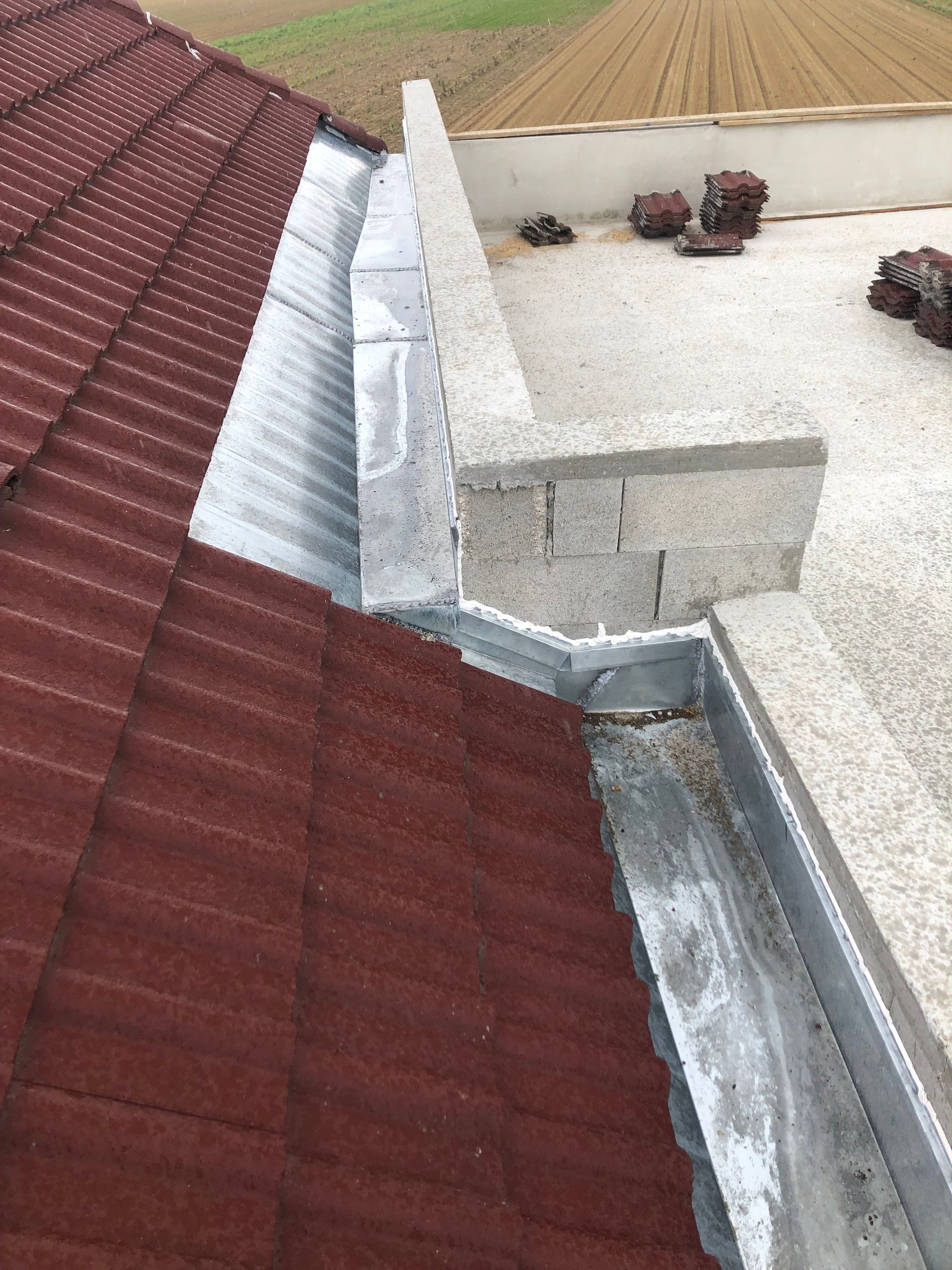 Coin de toit avec bardeaux rouges, solins métalliques et parapet en béton à côté d'une zone de toit en gravier.