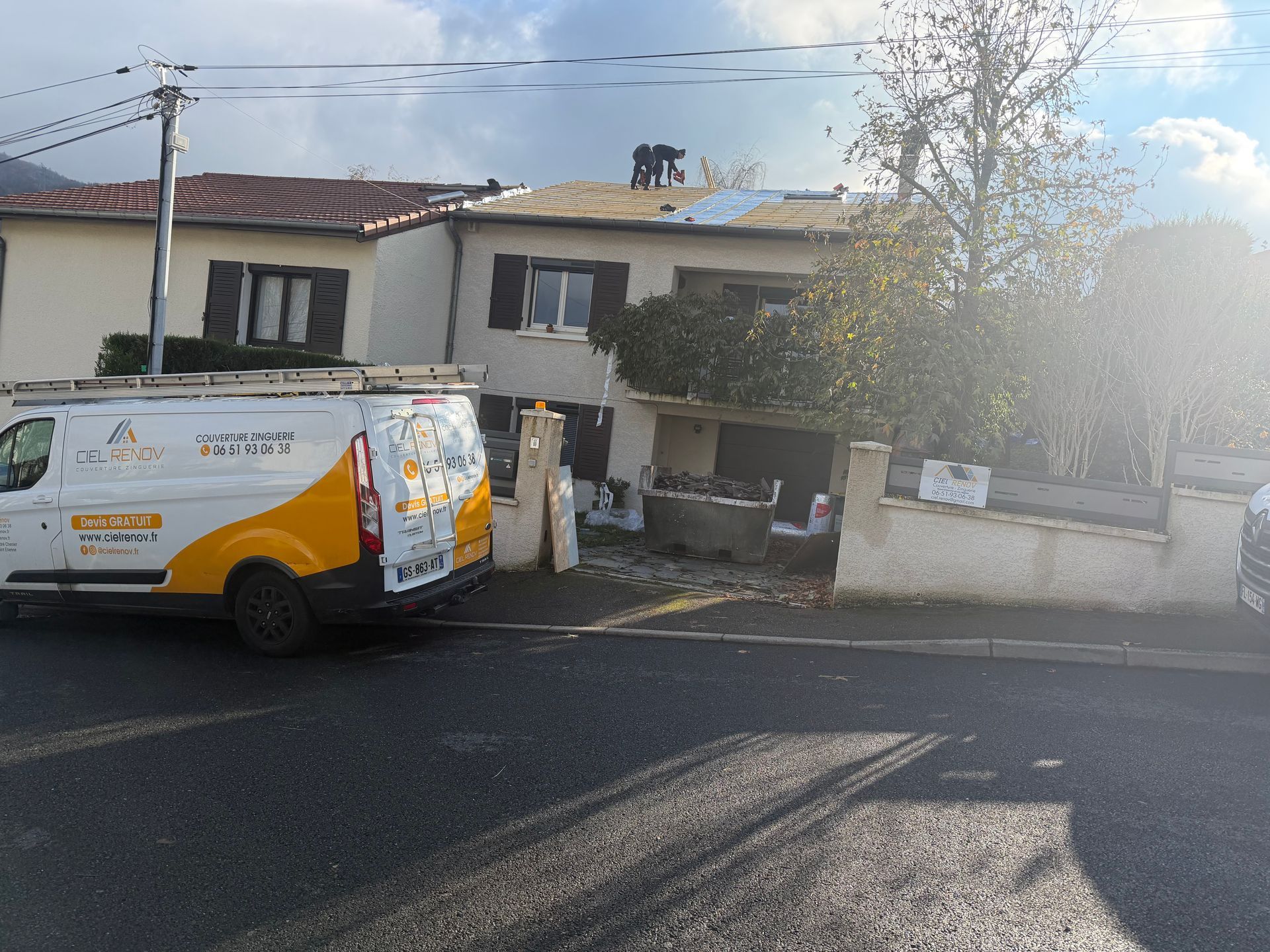 Une camionnette utilitaire blanche est garée devant une maison, le soleil éblouissant sur le côté droit.